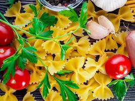 pasta farfalle, vlindervorm, tomaten, sjalotten, knoflook, peterselie op donkere achtergrond, bovenaanzicht, close-up foto