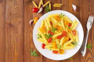 penne pasta met gele en rode tomaten versierd met basilicum op houten ondergrond, caloriearm dieetvoedsel, kopieer ruimte foto