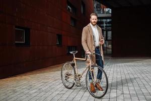 jonge man met fiets met een smartphone voorkant van het gebouw op zoek naar camera. foto