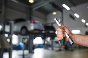 de hand van een autoreparateur met sleutels en een speciaal gereedschap op de achtergrond van het servicegebied. een monteur in een autoservicestation in uniform. kopieer ruimte foto