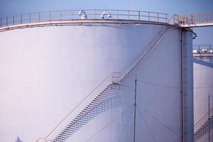 grote industriële tanks voor benzine en olie met blauwe sky.fuel-tanks op het tankpark. metalen trap aan de zijkant van een industriële oliecontainer. trap op grote brandstoftank foto