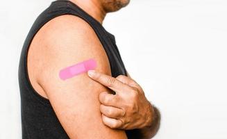 de roze pleister is bevestigd aan de arm van de man. concept voor eerste hulp na coronavirus covid-19 vaccinatie, en professioneel, medisch, naald, bloed, kanker. close-up, witte onscherpe achtergrond foto