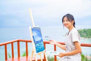 jong meisje met een penseeltekening op canvaspapier, bij een prachtig landschapszicht op koh tao thailand. foto