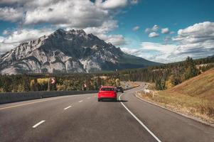 roadtrip met auto rijden op de weg met rotsachtige bergen in het herfstbos in het nationale park van banff foto