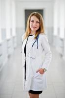 portret van een jonge aantrekkelijke arts in witte jas met stethoscoop poseren in het ziekenhuis. foto