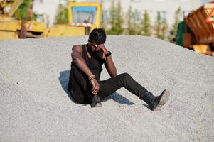 aantrekkelijke zwarte Afro-Amerikaanse man in zwarte spier shirt poseren op de stapel grind in industriële zone. foto
