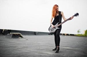 roodharige punkmeisjeskleding op zwart met basgitaar op het dak. foto