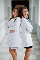 twee mooie vrouwelijke artsen of medisch personeel in witte jassen poseren in het ziekenhuis. foto
