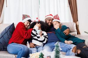 gelukkige familie heeft plezier om thuis samen op de bank te zitten. vrolijke jonge gezin met kinderen lachen. Afro-Amerikaanse familie foto