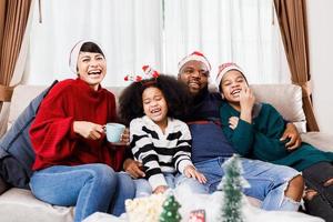 gelukkige familie heeft plezier om thuis samen op de bank te zitten. vrolijke jonge gezin met kinderen lachen. Afro-Amerikaanse familie foto