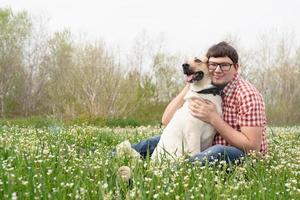 gelukkige man zit met gemengd ras herdershond op groen gras in Lentebloemen foto