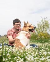 gelukkige man zit met gemengd ras herdershond op groen gras in Lentebloemen foto