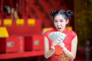 aziatische vrouw in chinese klederdracht houdt geld vast voor het chinese nieuwjaarsevenement foto