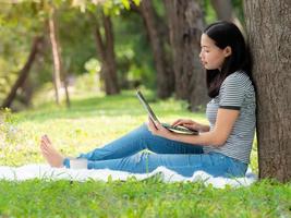 een mooie Aziatische vrouw ontspant in de tuin, leest en zoekt leerinformatie van internet foto