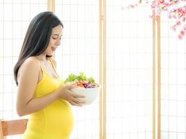 een mooie zwangere vrouw in een Japanse kamer die een groentesalade bereidt om te eten voor een goede gezondheid foto