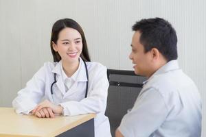 jonge aziatische professionele vrouwelijke arts goed humeur glimlach suggereert gezondheidsoplossingen voor oudere mannelijke patiënten in de onderzoekskamer van het ziekenhuis. foto