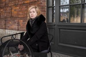 blondine in jas met bontkraag zit aan tafel en verwarmt haar handen boven gloeiende kolen. foto