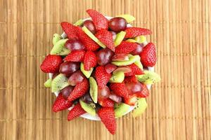 fruitsalade met aardbeien, druiven en kiwi op rotan backgro