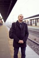 treinstation. volwassen man in zakelijke kleding en jas staat op platform foto
