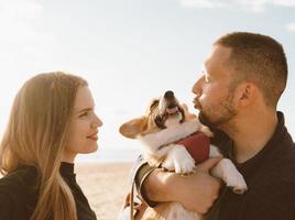 jonge gelukkige paar met hond wandelen op het strand. mooi meisje en jongen en corgi puppy foto