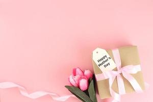 moederdag achtergrond. bovenaanzicht van geschenkdoos met roze strikken - lang lint en mooie bloemen op pastelroze achtergrond met kopieerruimte foto