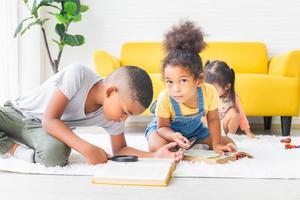 klein kind meisje en jongen leesboek met vergrootglas op de vloer, gelukkige kinderen spelen in de woonkamer foto