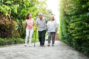 gelukkige familie die samen in de tuin loopt. oude ouderen die een wandelstok gebruiken om het evenwicht te helpen lopen. concept van liefde en zorg voor het gezin en een ziektekostenverzekering voor het gezin foto