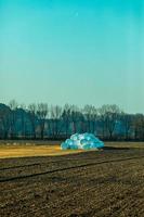 stapel in plastic verpakte hooibalen door geploegd veld foto