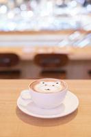 schattige beer latte warme koffie in witte kop op houten tafel, lees om te serveren. foto