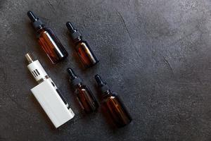 vaping apparaat e-sigaret elektronische sigaret en vloeibare flessen op donkere zwarte stenen leisteen achtergrond. vape-apparaat voor alternatief roken. vapen winkelconcept. gadget voor damper. accessoires voor dampen. foto