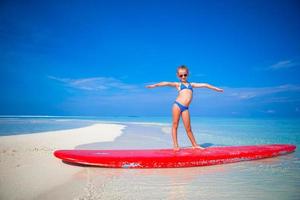 klein schattig meisje oefent surfpositie op het strand foto