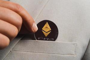 gouden ethereum eth inbegrepen bij cryptocurrency op pakzak zakenman pikt op met vingers die een bruin colbert dragen. zet en geef aan mij en detail van de vezels van de prachtige achtergrond foto