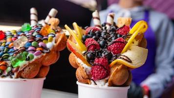 bubbelwafels met frambozen, chocolade en marshmallow in witte papieren bekers worden verkocht op een open keukenvoedselfestival. Hongkongse wafels. foto