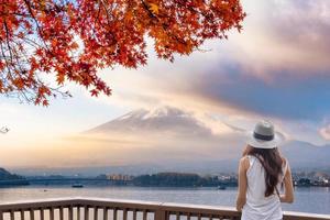 jonge aziatische vrouw die 's ochtends op een houten balkon staat en naar de berg Fuji-san kijkt door mist met rode esdoorndekking foto