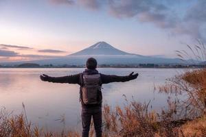 Aziatische jonge man staat op zoek naar de berg Fuji op het Kawaguchiko-meer bij zonsopgang? foto