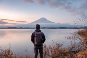 jonge Aziatische man staat op zoek naar de berg Fuji op het Kawaguchiko-meer bij zonsopgang? foto