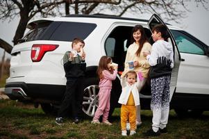 moeder met kinderen drinkt thee buiten in de buurt van witte suv-auto. foto