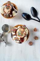 Vanille-ijslepels met kleurrijke snoepstukjes en chocoladesiroop in wafelkegelkom op rustieke witte achtergrond foto