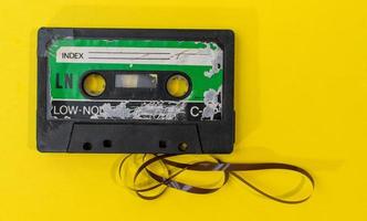 oude retro cassettebandje met grunge label omgeven door getrokken tape stapel op gele achtergrond plat lag foto