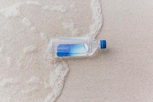 fles drinkwater op het strand in de buurt van de zee. foto