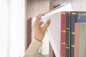 close-up shot hand van jonge vrouw die boek uit bibliotheek boekenplank neemt foto