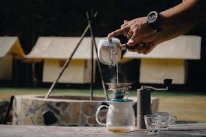 druppel koffie man giet water op koffiedik met filter in het kamp. foto