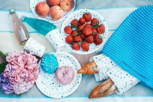 picknickset met aardbeien, stokbrood, drankjes, gebreide tas voor picknick met zomerbloemen op plaid foto