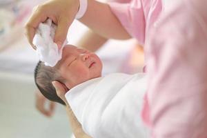 Aziatische pasgeboren baden door zijn moeder, babyjongen foto
