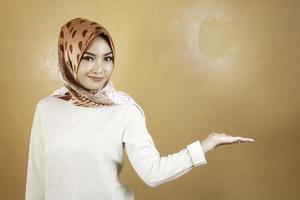 vrolijke jonge moslim aziatische vrouw die naar de kant wijst om de ruimte met een glimlach te kopiëren foto