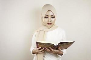 jonge aziatische moslimvrouw die een hoofddoek draagt die de koran leest foto