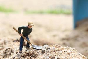 miniatuur werkpop met schop om te werken, mijnwerker man aan het werk klein figuur speelgoedmodel grond graven of tuinieren foto