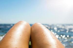 gladde gebruinde vrouwelijke benen in de spray van water op het strand tegen de achtergrond van de zee. bruiningsproducten, zonnebrandbescherming, huidverzorging, ontharing, strandvakanties. kopieer ruimte foto