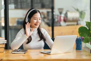 lachende vrouw met een draadloze koptelefoon die aan het typen is op een notebook zit aan de balie op de kantoorwerkplek. geniet van het e-learningproces, eenvoudig comfortabel gebruik van de applicatie, luister naar muziek tijdens het werkdagconcept foto