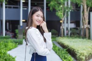 Aziatische zakenvrouw die een wit overhemd draagt en glimlacht terwijl ze buiten kantoor werkt foto